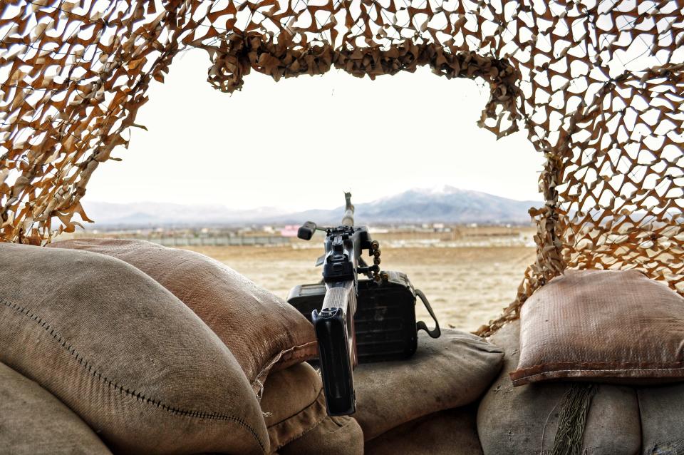 The view from a machine gun position in Afghanistan, including tan sandbags and a desert military camouflage net. Afghan landscape and mountain slightly blurred in background to give depth. War, ISAF, NATO