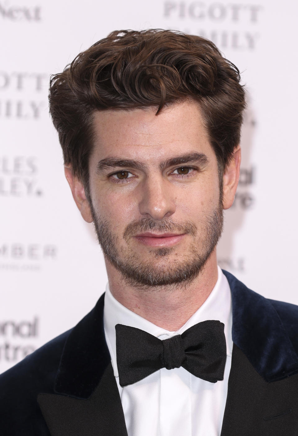 Andrew Garfield poses at an event in a tuxedo with a bow tie