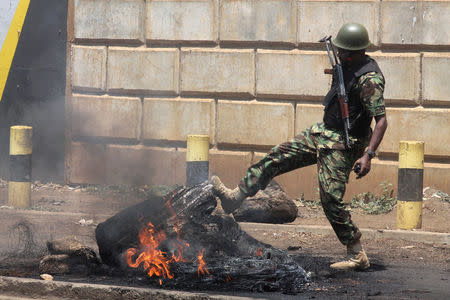 A Kenyan policeman kicks a burning tire set on fire by protesters supporting opposition leader Raila Odinga during clashes in Kisumu, Kenya August 11, 2017. REUTERS/James Keyi