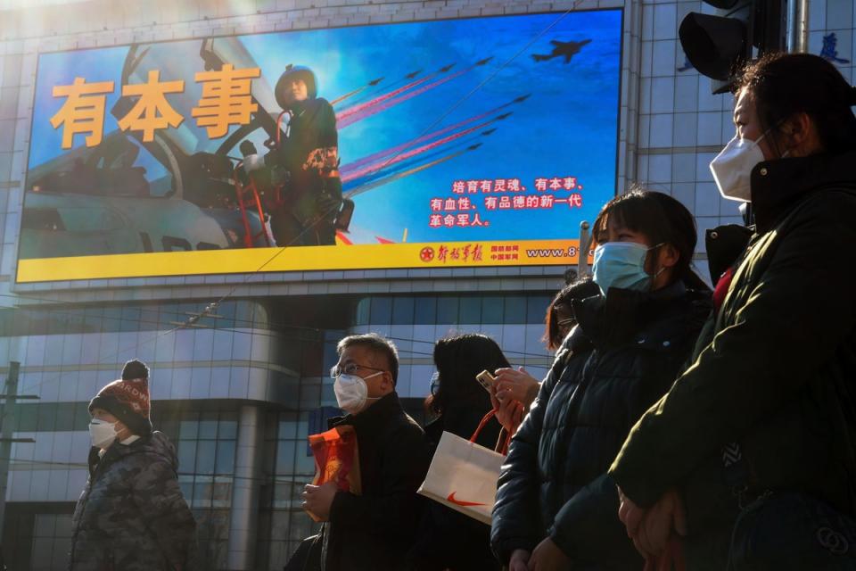 Residents wearing face masks wait to cross a traffic intersection near a large screen promoting the Chinese People's Liberation Army Airforce (AP)