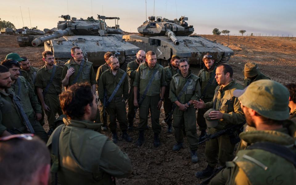 Israeli soldiers are briefed beside two tanks on the Gaza border ahead of the expected expiry of the truce early tomorrow
