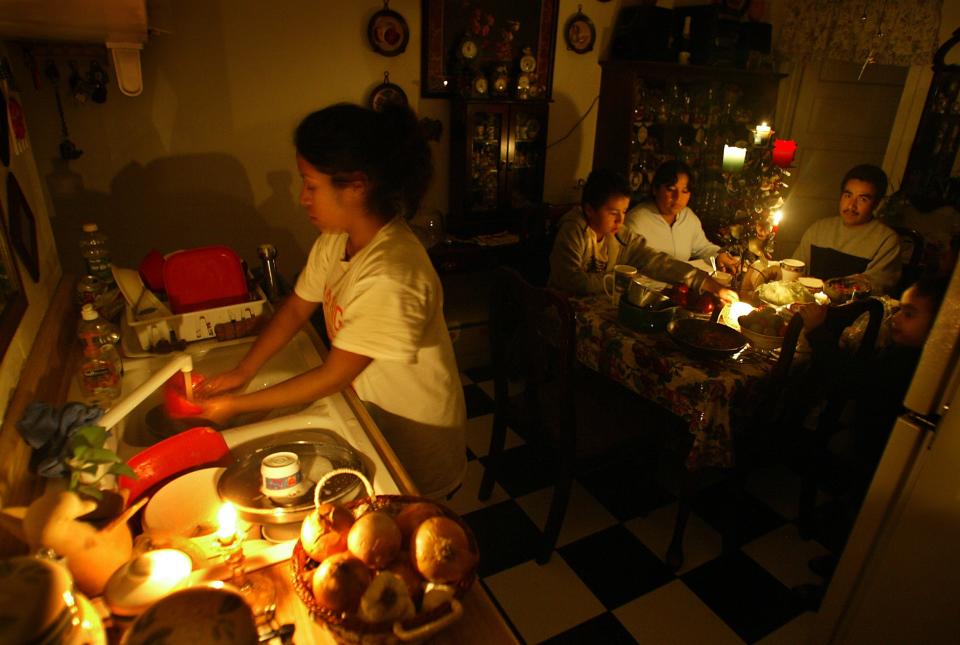 File: A teen does dishes by candlelight as her family relax after dinner by candlelight due to power outages caused by strong Santa Ana winds in Southern California.