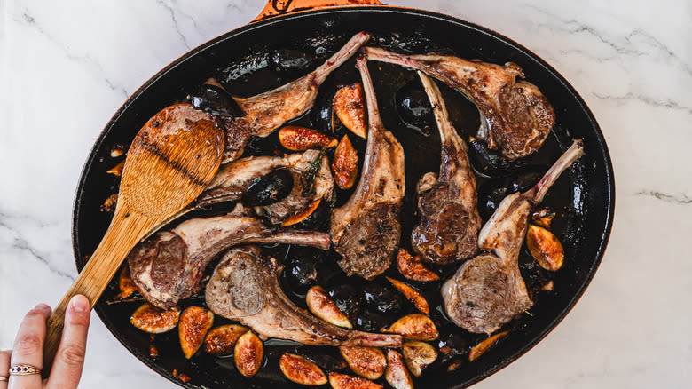 A hand stirring roasted lamb chops with thyme and figs