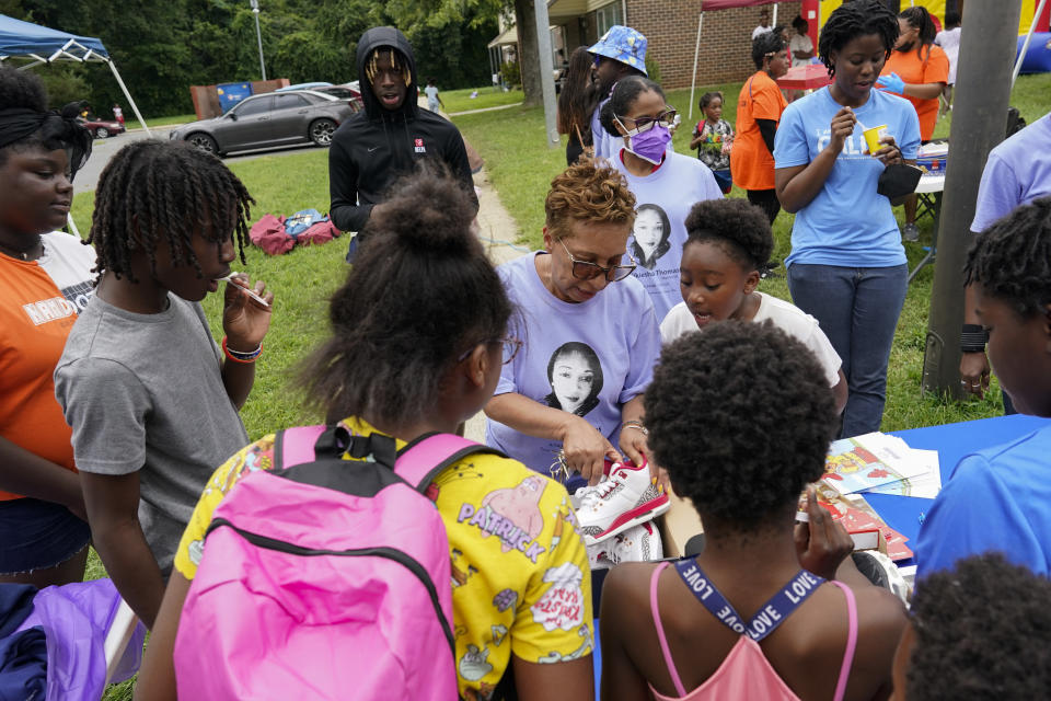 Nikiesha Thomas's aunt Venice Mundle-Harvey, center, and cousin, Nashonie Chang, behind in face mask, hand out donated school supplies and shoes during a Back To School Block Party in the Robinwood Community of Annapolis, Md., Sunday, Aug. 21, 2022. Nikiesha Thomas was shot and killed by her ex-boyfriend just days after filing for a protective order. (AP Photo/Carolyn Kaster)