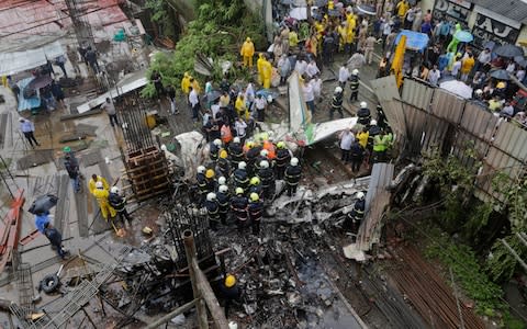 Rescuers stand amid the wreckage of a private chartered plane that crashed in Ghatkopar area, Mumbai - Credit: Rajanish Kakade/AP