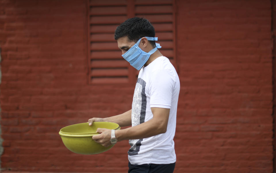 Un hombre con barbijo lleva con cuidado un cuenco lleno de alimentos que recibió en un comedor popular en las afueras de Buenos Aires, Argentina, el miércoles 25 de marzo de 2020. (AP Foto / Natacha Pisarenko)