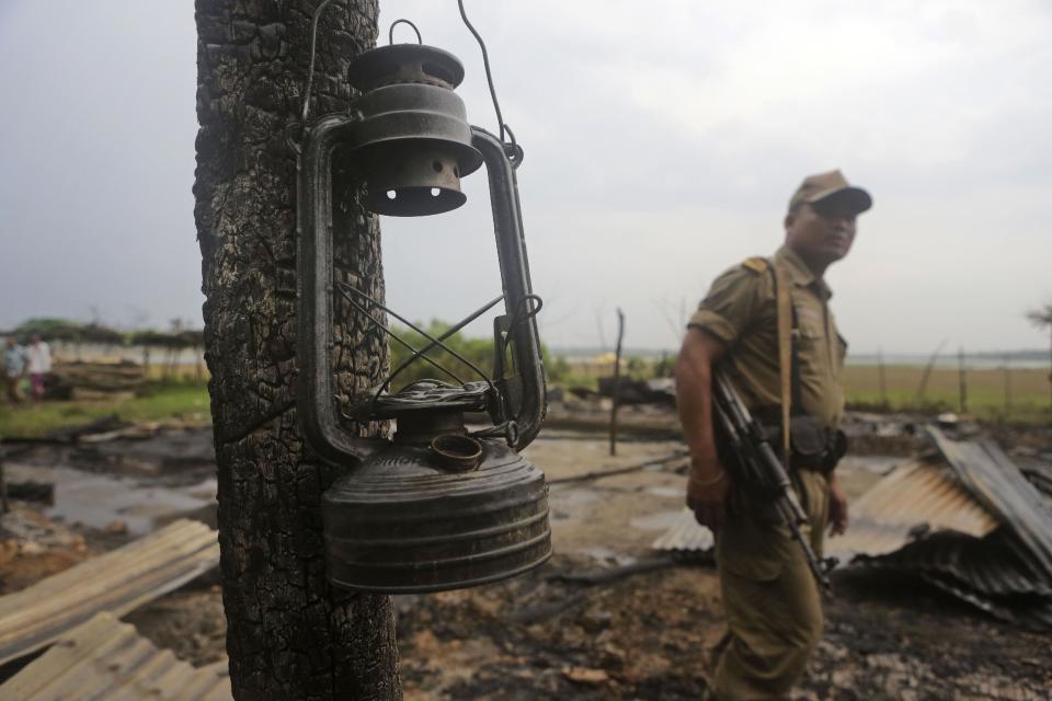 A security officer walks past a lantern hanging by the post of a burnt house at the violence-affected village of Khagrabari, in the northeastern Indian state of Assam, Saturday, May 3 2014. Police in India arrested 22 people after separatist rebels went on a rampage, burning homes and killing dozens of Muslims in the worst outbreak of ethnic violence in the remote northeastern region in two years, officials said Saturday. (AP Photo/Anupam Nath)