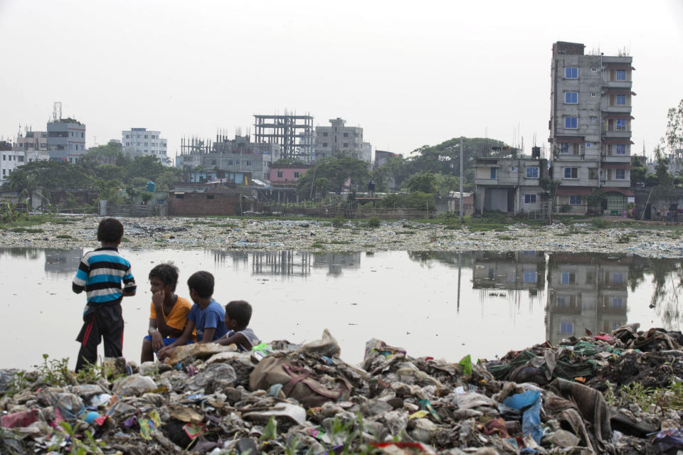 FILE - In this June 4, 2018, file photo, Bangladeshi children sit on garbage piled up by the river Buriganga in Hazaribagh area in Dhaka, Bangladesh. A new report by the United Nations children’s agency says the lives and futures of more than 19 million Bangladeshi children are at risk from colossal impacts of devastating floods, cyclones and other environmental disasters linked to climate change. The UNICEF report released Friday, April 5, 2019 said the tally includes Rohingya refugee children from Myanmar who are living in squalid camps in southern Bangladesh.( AP Photo/A.M. Ahad, File)