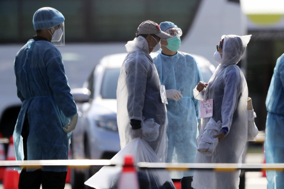 An official in protective suits escort the foreign passengers disembarked from the quarantined Diamond Princess cruise ship before boarding to buses at a port in Yokohama, near Tokyo, Friday, Feb. 21, 2020. Passengers tested negative for COVID-19 started disembarking since Wednesday. (AP Photo/Eugene Hoshiko)