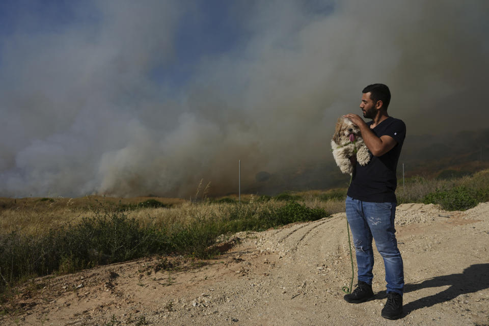 A man holds his dog next to a field ablaze after being struck by a rocket fired from the Gaza Strip, near the southern Israeli city of Sderot, Tuesday, May 2, 2023. The Israeli military says that Palestinian militants in Gaza have fired a barrage of rockets following the death of Khader Adnan, a high-profile Palestinian prisoner in Israeli custody after a nearly three-month-long hunger strike. (AP Photo/Tsafrir Abayov)