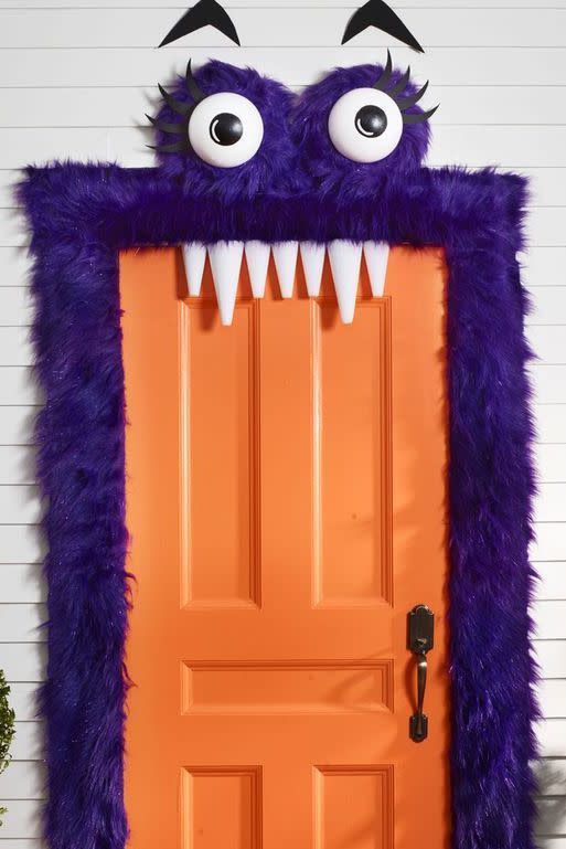 <p>This furry purple exterior means you don't have to worry about scaring the youngest trick-or-treaters! (And those friendly eyebrows and teeth totally steal the show.)</p><p><strong>Make the Monster Door:</strong> To make eyes, paint black circles on two 8" foam half balls; let dry. Paint on white highlight. Cut eyelashes and eyebrows from black foam. Cut two 16" squares and hot-glue each around a 12" foam wreath, from three yards faux purple fur. Glue eyeballs in center and eyelashes across top. Add a string across back of each eye for hanging. Frame door with strips of fur using pieces of double-sided tape. <br></p><p>Use Command Hooks to hang eyes above door. Tack or tape eyebrows in place. For teeth, use foam cones, and then attach to top of door frame with double-sided tape.  </p>