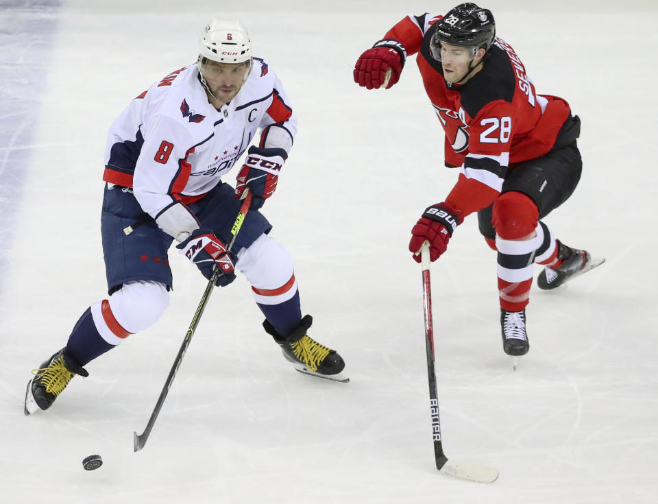 Washington Capitals left wing Alex Ovechkin (8) moves the puck as New Jersey Devils defenseman Damon Severson (28) defends during the first period of an NHL hockey game Sunday, Feb. 28, 2021, in Newark, N.J. (Andrew Mills/NJ Advance Media via AP)