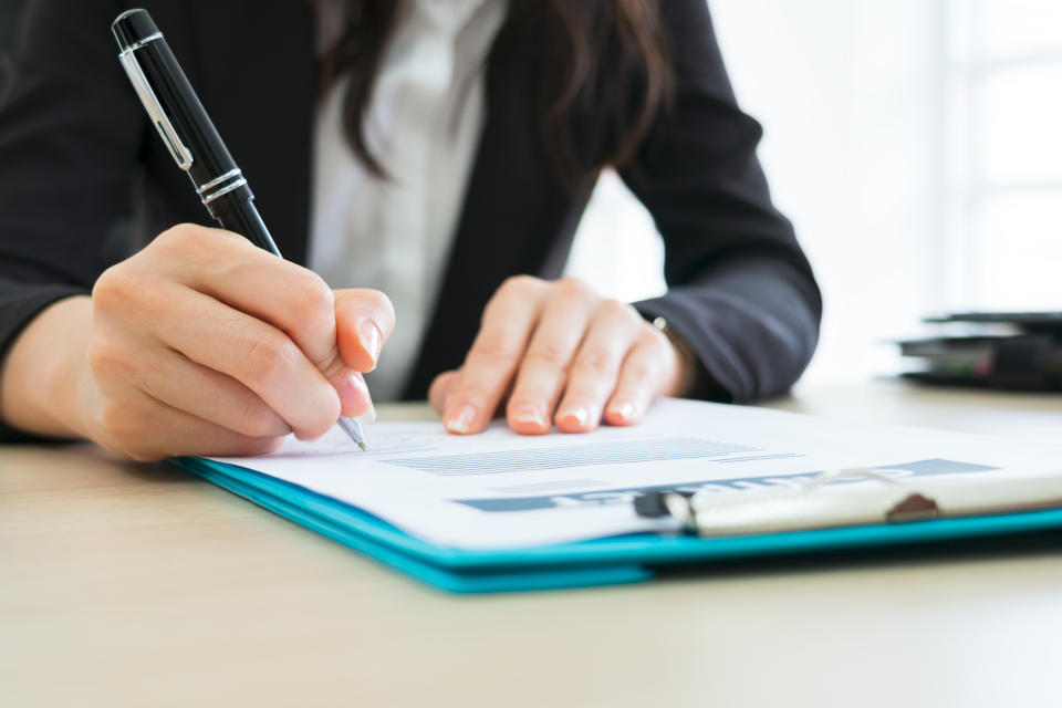 Person writing in a document on a clipboard at a desk