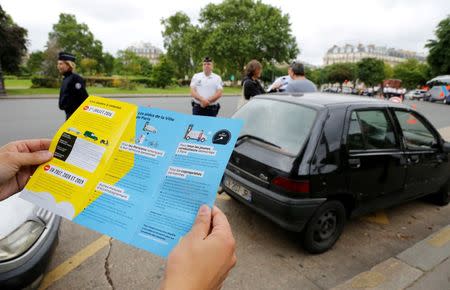 A man holds a leaflets as French police speaks to a driver with a car older than 20 years to explain a new law to fight air pollution at the Place de la Nation square in Paris, France, July 1, 2016. REUTERS/Jacky Naegelen