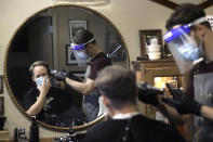 Vin Norton, of Wellesley, Mass., left, gets his hair cut by barber Cristian Lopez, of Sherborn, Mass., at Barber Walter's barbershop, as they both wear masks out of concern for the coronavirus, Tuesday, May 26, 2020, in Wellesley. Hair salons and barbershops were allowed to open Monday, May 25 in Massachusetts after being closed for about two months due to the coronavirus pandemic. (AP Photo/Steven Senne)