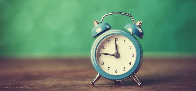 An alarm clock sits on a table with a green background.