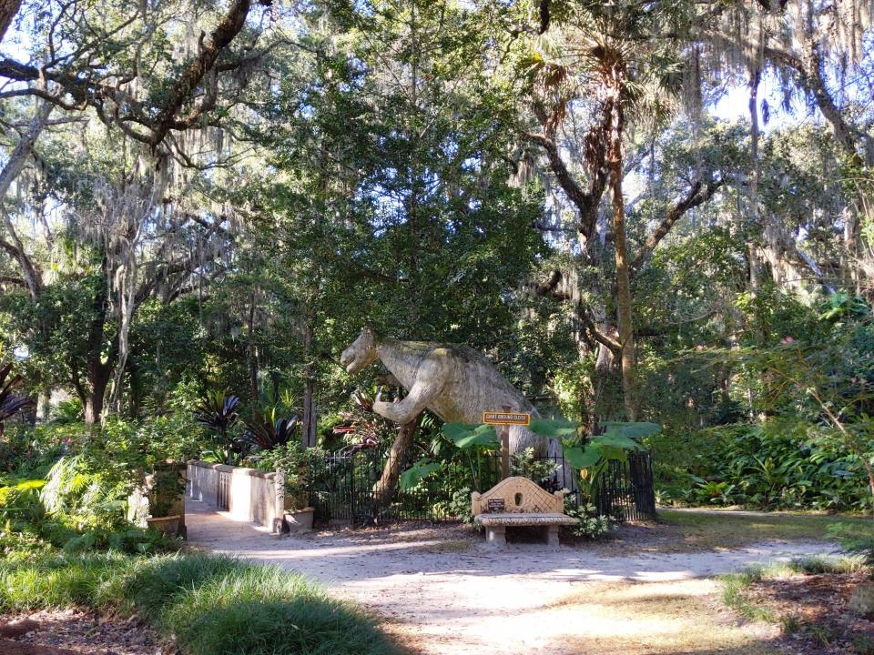 A lush leafy park with a dinosaur statue.