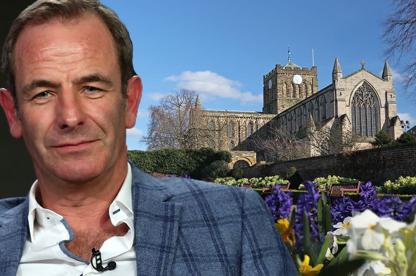 man in blue suit jacket next to hexham abbey and spring flowers