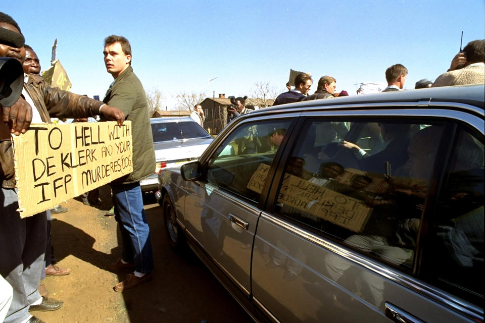 FILE - President F.W. de Klerk, right, behind window, watches protesters while on a visit to Boipatong, South Africa, June 20, 1992, following violence in the area. South Africa is engrossed in debate over the legacy of apartheid's last president, de Klerk, who died last week at 85. (AP Photo/Greg Mariovich, File)