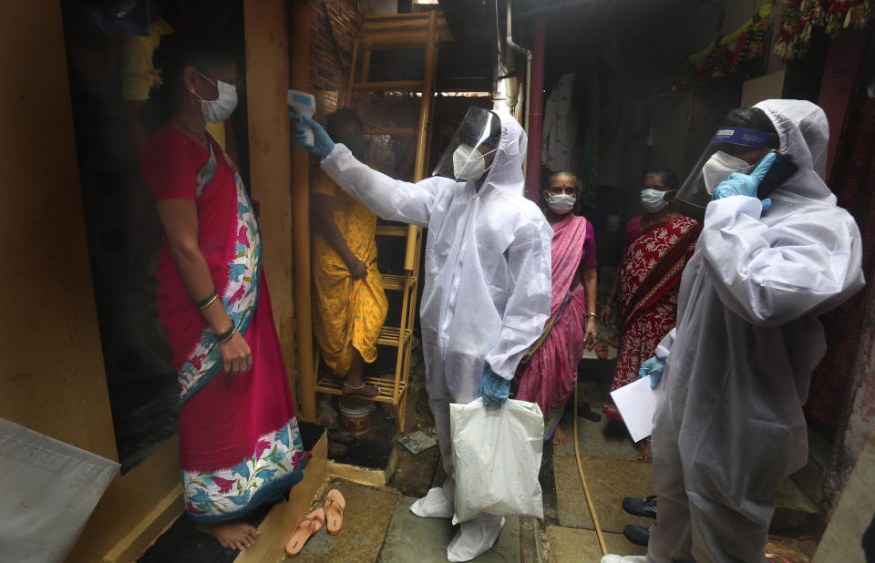 A health worker checks the body temperature of a resident, as others await their turn during a free medical checkup in a slum in Mumbai, India, Sunday, June 28, 2020. India is the fourth hardest-hit country by the COVID-19 pandemic in the world after the U.S., Russia and Brazil. (AP Photo/Rafiq Maqbool)