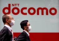 Passersby wearing protective face masks walk past in front of NTT Docomo shop in Tokyo, Japan