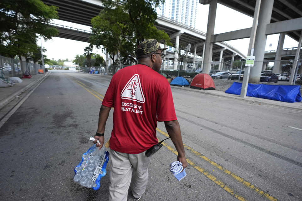 FILE - Ricky Leath, an outreach specialist with the City of Miami, walks through a homeless encampment as he works with the Miami-Dade County Homeless Trust to distribute bottles of water and other supplies to the homeless population, helping them manage high temperatures, May 15, 2024, in Miami. The Miami-Dade government and the local National Weather Service office team up to treat heat like hurricanes and emphasize advanced preparations. (AP Photo/Lynne Sladky, File)