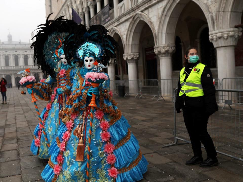 A policewoman wearing a protective mask stands next to carnival revellers at Venice Carnival, which the last two days of, as well as Sunday night's festivities, have been cancelled because of an outbreak of coronavirus, in Venice, Italy February 23, 2020.