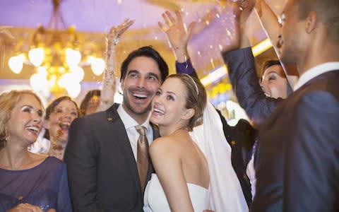 Friends throwing confetti over bride and groom at wedding reception - Credit: Caiaimage/Tom Merton