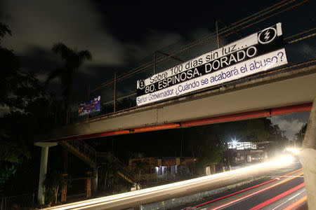 Cars drive through a neighbourhood without electricity after the electrical grid was damaged by Hurricane Maria last September, in Dorado, Puerto Rico January 22, 2018. The sign on the bridge reads "Over 100 days without light, neighbourhood Espinosa, Dorado, Mr. Governor, when will the abuse be over?" REUTERS/Alvin Baez