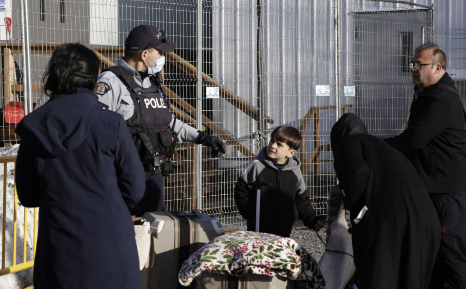 A Canadian police officer speaks with a migrant family from Afghanistan who walked across the non-official Roxham Road border crossing north of Champlain, N.Y.,, on Friday, March 24, 2023. A new US-Canadian migration agreement closes a loophole that has allowed migrants who enter Canada away from official border posts to stay in the country while awaiting an asylum decision. (AP Photo/Hasan Jamali)
