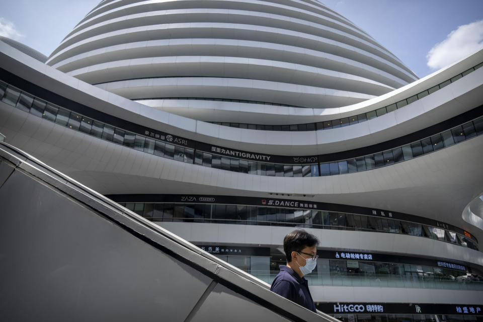 A man wearing a face mask walks through a shopping and office complex in Beijing, Thursday, June 30, 2022. (AP Photo/Mark Schiefelbein)