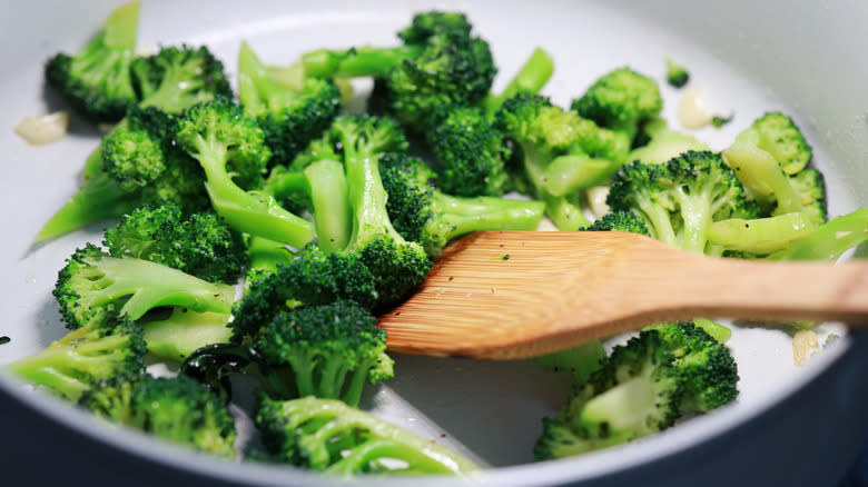 Broccoli florets in pan with wooden spatula