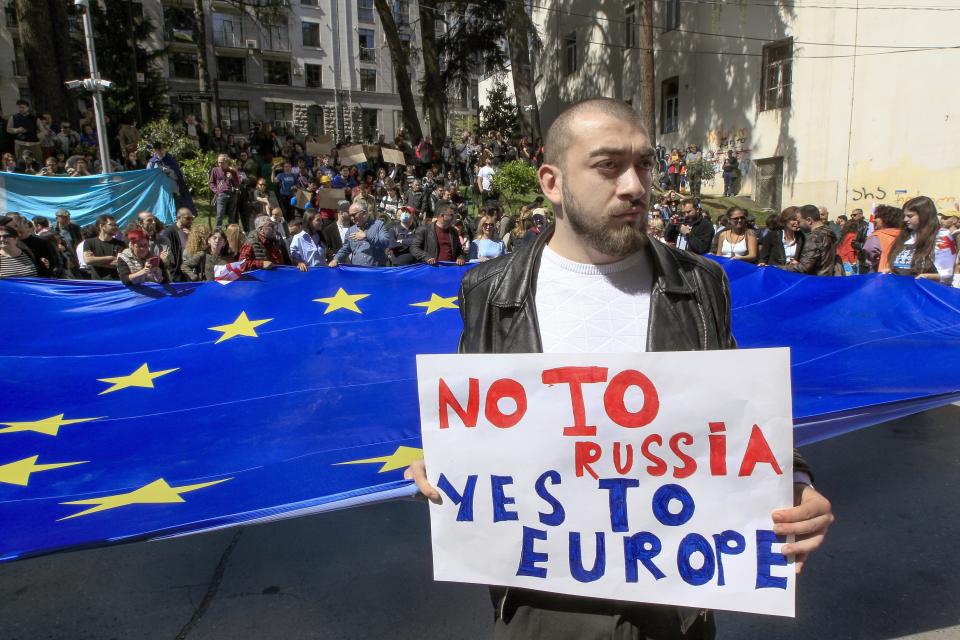 A man stands in front of protestors with a giant EU flag outside the parliament building in Tbilisi, Georgia, on Monday, April 15, 2024 to protest against the "the Russian law" as it is similar to a law that Russia uses to stigmatize independent news media and organizations seen as being at odds with the Kremlin. The governing party in the country of Georgia has submitted to parliament a draft law calling for media and non-commercial organizations to register as being under foreign influence if they receive more than 20% of their budget from abroad. (AP Photo/Shakh Aivazov)