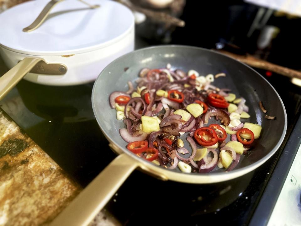 A pan filled with cooking chile peppers and sliced red onions next to a white pot with a lid on it