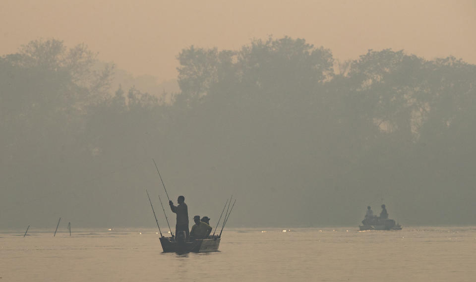 Men fish in the Cuiaba river amid smoke from fires at the Encontro das Aguas park at the Pantanal wetlands near Pocone, Mato Grosso state, Brazil, Sunday, Sept. 13, 2020. A vast swath of a vital wetlands is burning in Brazil, sweeping across several national parks and obscuring the sun behind dense smoke. (AP Photo/Andre Penner)