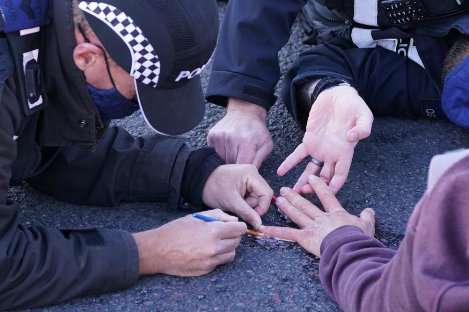 Police officers remove a protester glued to the road at an Insulate Britain roadblock on the M25 (PA) (PA Archive)