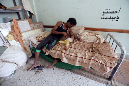 A man sits on a bed with a child, at a school to which they have been evacuated from a village near Hodeidah airport amid fighting between government forces and Houthi fighters in Hodeidah, Yemen June 18, 2018. REUTERS/Abduljabbar Zeyad