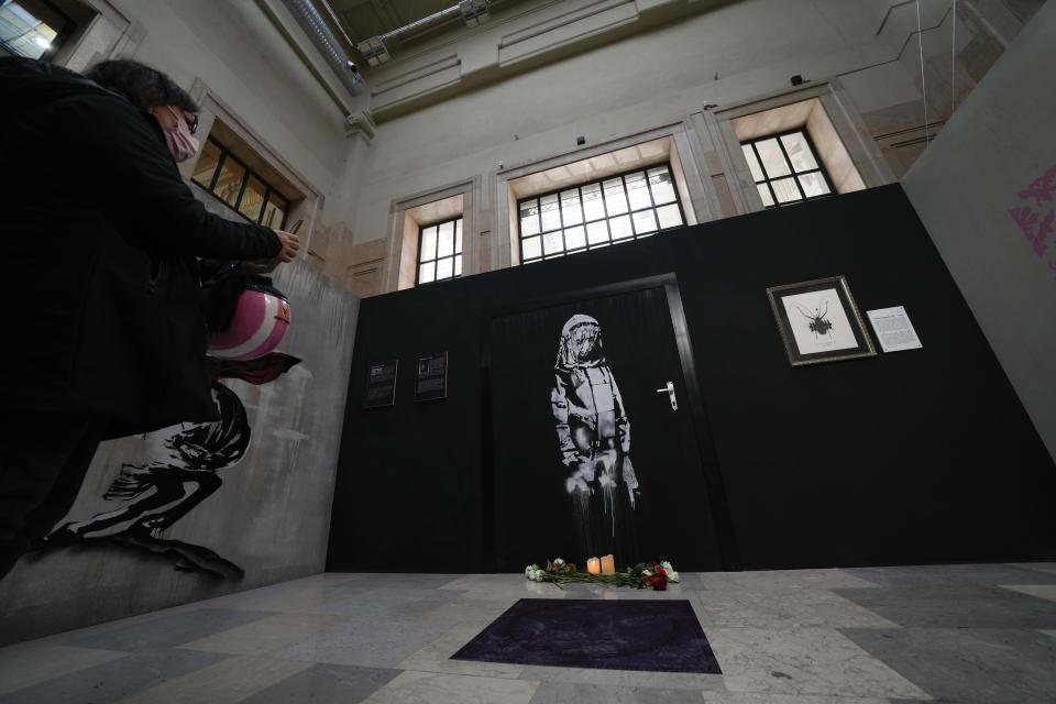 A visitor takes pictures of "Bataclan", a reproduction of a mural by British artist Banksy, during the unveiling of the "The World of Banksy, The Immersive Experience" exhibition, in Milan, Italy, Thursday, Dec. 2, 2021. An exhibition of 130 works by British street artist Banksy opens Friday in a gallery space inside Milan's Central train Station. The exhibition unveiled on Thursday includes 30 never before seen works by Bansky and highlights pieces by young unknown artists from all over Europe. (AP Photo/Luca Bruno)