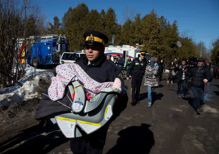 A Royal Canadian Mounted Police (RCMP) officer carries a child in a carseat as the mother is escorted behind to a waiting RCMP vehicle after crossing the U.S.-Canada border into Hemmingford, Canada February 20, 2017. REUTERS/Christinne Muschi