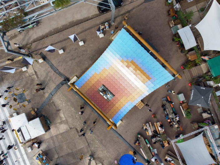 A high aerial view of the solar pavilion reveals a design that looks like a sun rising into a crisp blue sky.