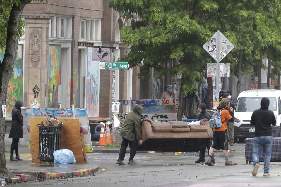 Protesters move a couch and other items to replace concrete barricades cleared by Seattle Department of Transportation workers at the intersection of 10th Ave. and Pine St., Tuesday, June 30, 2020 at the CHOP (Capitol Hill Occupied Protest) zone in Seattle. The area has been occupied by protesters since Seattle Police pulled back from their East Precinct building following violent clashes with demonstrators earlier in the month. (AP Photo/Ted S. Warren)