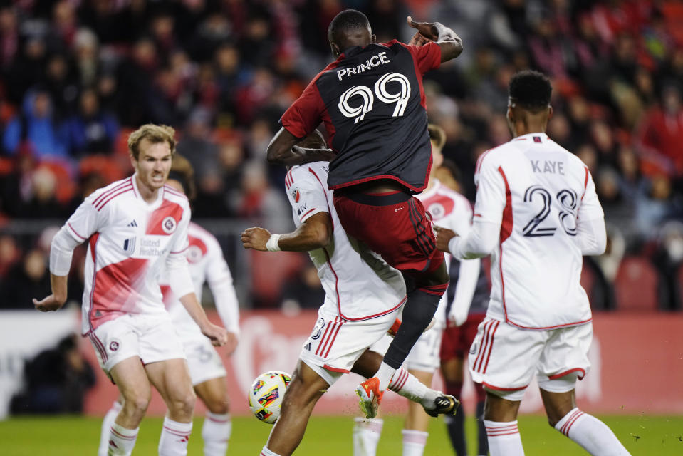 Toronto FC's Prince Osei Owusu (99) scores over New England Revolution's Andrew Farrell, center, as Revolution's Mark-Anthony Kaye (28) watches during the second half of an MLS soccer match Saturday, April 20, 2024, in Toronto. (Frank Gunn/The Canadian Press via AP)