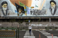 In this Friday, April 3, 2020 photo, a man crosses an empty street under portraits of the late Iranian revolutionary founder Ayatollah Khomeini, right, and Supreme Leader Ayatollah Ali Khamenei, left, in Tehran, Iran. Due to the virus and the COVID-19 illness it causes, life has changed dramatically on Tehran's main highways, in the narrow corridors of its historical Grand Bazaar and in the public spaces under portraits of its leaders. (AP Photo/Ebrahim Noroozi)