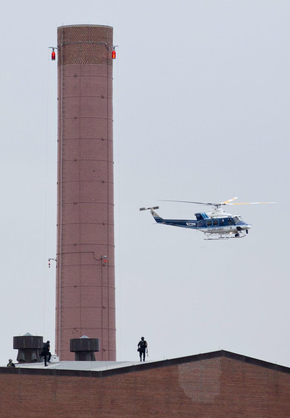 A police helicopter flies overhead as police walk on the roof of a building as they respond to a shooting at the Washington Navy Yard in Washington September 16, 2013. A gunman shot five people at the U.S. Navy Yard on Monday, including two law enforcement officers, and the shooter was being sought in a building housing the Naval Sea Systems Command headquarters, officials said. (REUTERS/Joshua Roberts)