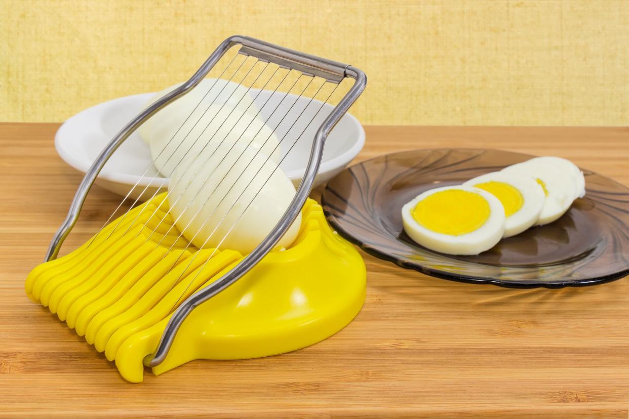 Egg slicer with egg in it, sliced and  whole peeled boiled eggs on a different saucers on a wooden bamboo surface at selective focus