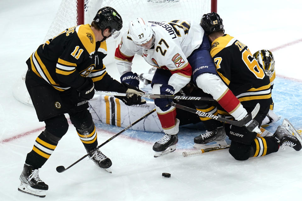 Florida Panthers center Eetu Luostarinen (27) tries to gain control of the puck while pressured by Boston Bruins center Trent Frederic (11) and defenseman Jakub Zboril (67) during the first period of an NHL hockey game, Monday, Oct. 17, 2022, in Boston. (AP Photo/Charles Krupa)
