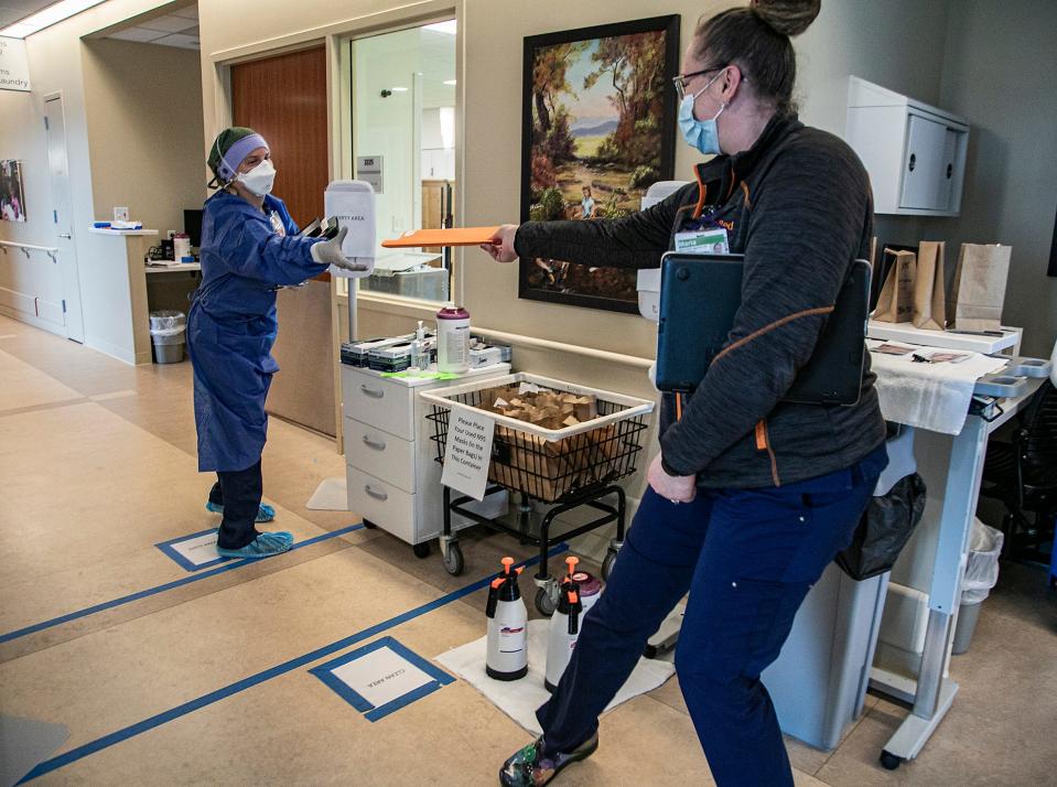 Nursing director Maria Opoku-Agyeman, right, hands off a medical file from the area in a hallway at the Mary Free Bed Rehabilitation Hospital in Grand Rapids that stops medical personnel from freely crossing without taking precautions in a wing converted to accommodate the rehabilitation of COVID-19 patients. The unit has been broken down into distinctive 'clean' and 'dirty' sides to help manage medical caretakers to don and doff personal protection equipment (PPE) before entering or leaving the COVID treatment side.