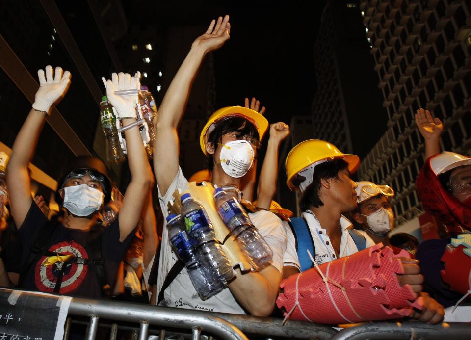 Pro-democracy protesters, protecting themselves with helmets, masks, foam pads and empty plastic bottles, raise their hands at riot police as a gesture of peace after they were told by visiting lawmakers not to charge the police defence line, at Mongkok shopping district in Hong Kong early October 20, 2014. The worst political crisis in Hong Kong since Britain handed the free-wheeling city back to China in 1997 entered its fourth week with no sign of a resolution despite talks scheduled on Tuesday between the government and student protest leaders. REUTERS/Liau Chung-ren (CHINA - Tags: POLITICS CIVIL UNREST)