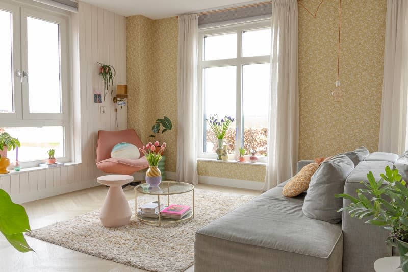 Circular glass coffee table holds vase with tulips in living room with gray modular sofa and pink accent chair.