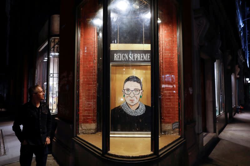 A person looks towards a painting in a storefront on Broadway of Associate Justice of the Supreme Court of the United States Ruth Bader Ginsburg who passed away in Manhattan, New York City